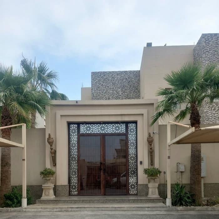مدخل فيلا بباب خشبي منقوش بين نخلتين